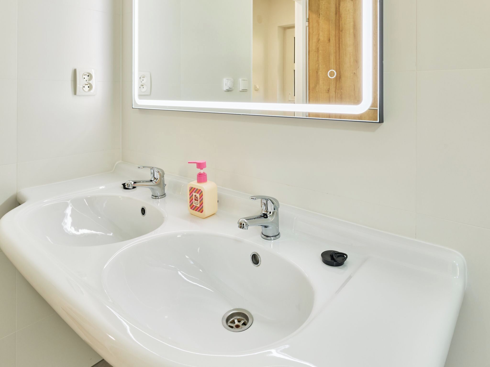 A bathroom with two sinks, a mirror, and a bottle of soap.