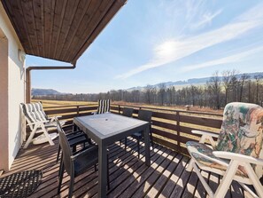 A wooden deck with a table and chairs, overlooking a rural landscape.