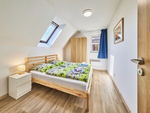 A bedroom with a skylight, a bed with a floral bedspread, a bedside table, a wardrobe, and a door with a handle.