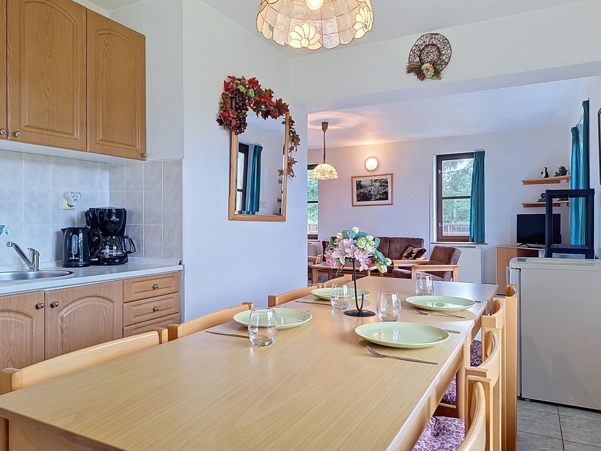 Una cucina moderna con mobili in legno, un tavolo da pranzo apparecchiato con piatti e bicchieri, e un angolo soggiorno con divano e televisore.