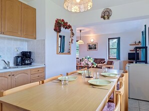 A modern kitchen with wooden cabinets, a dining table set with plates and glasses, and a living area with a sofa and a TV. - Green Valley Park Stárkov 7 by Interhome (Stárkov)