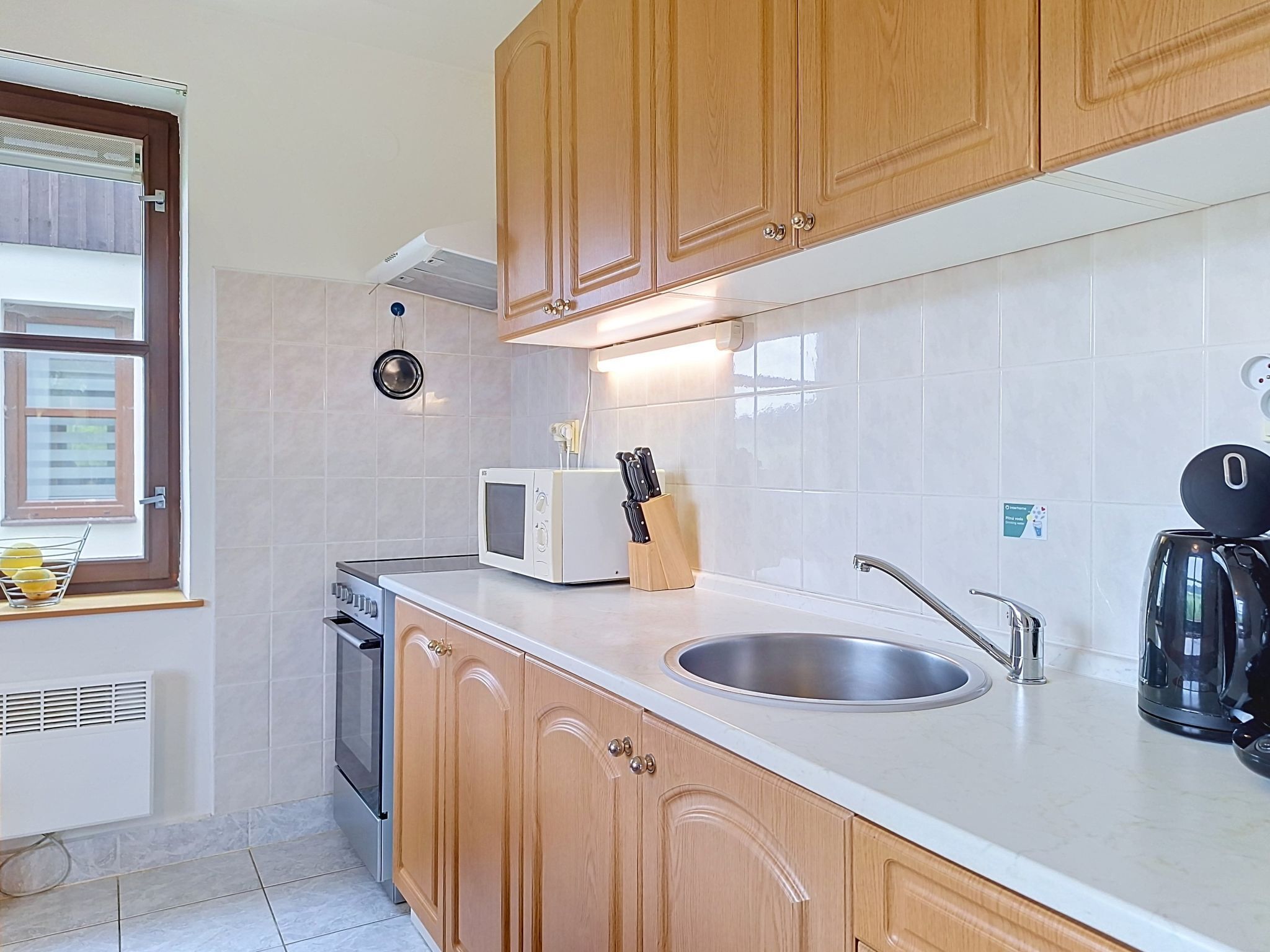 A kitchen with wooden cabinets, a microwave, a sink, and a kettle.