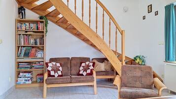 Un soggiorno con una scala in legno, un divano con cuscini decorati, una libreria e un tavolino.
