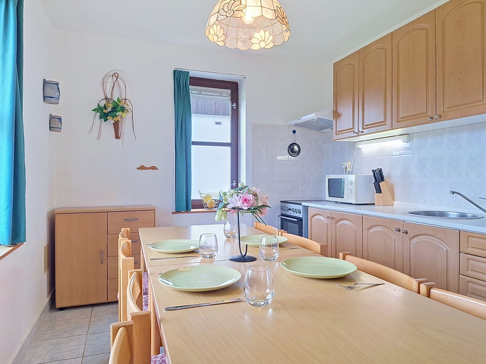 Una cocina moderna con armarios de madera, una mesa de comedor con platos y vasos, un microondas y un lavabo.