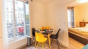 A small room with a dining table, two yellow chairs, a bed, and a window with a view of buildings.