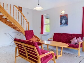 A room with a wooden staircase, a red sofa set, a wooden coffee table, and a painting on the wall.