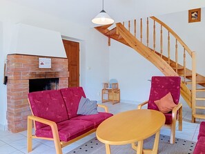 A living room with a brick fireplace, wooden staircase, red sofa, and a round wooden table.