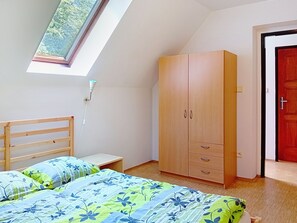 A bedroom with a skylight, a bed with floral bedding, a wardrobe, and a red door.