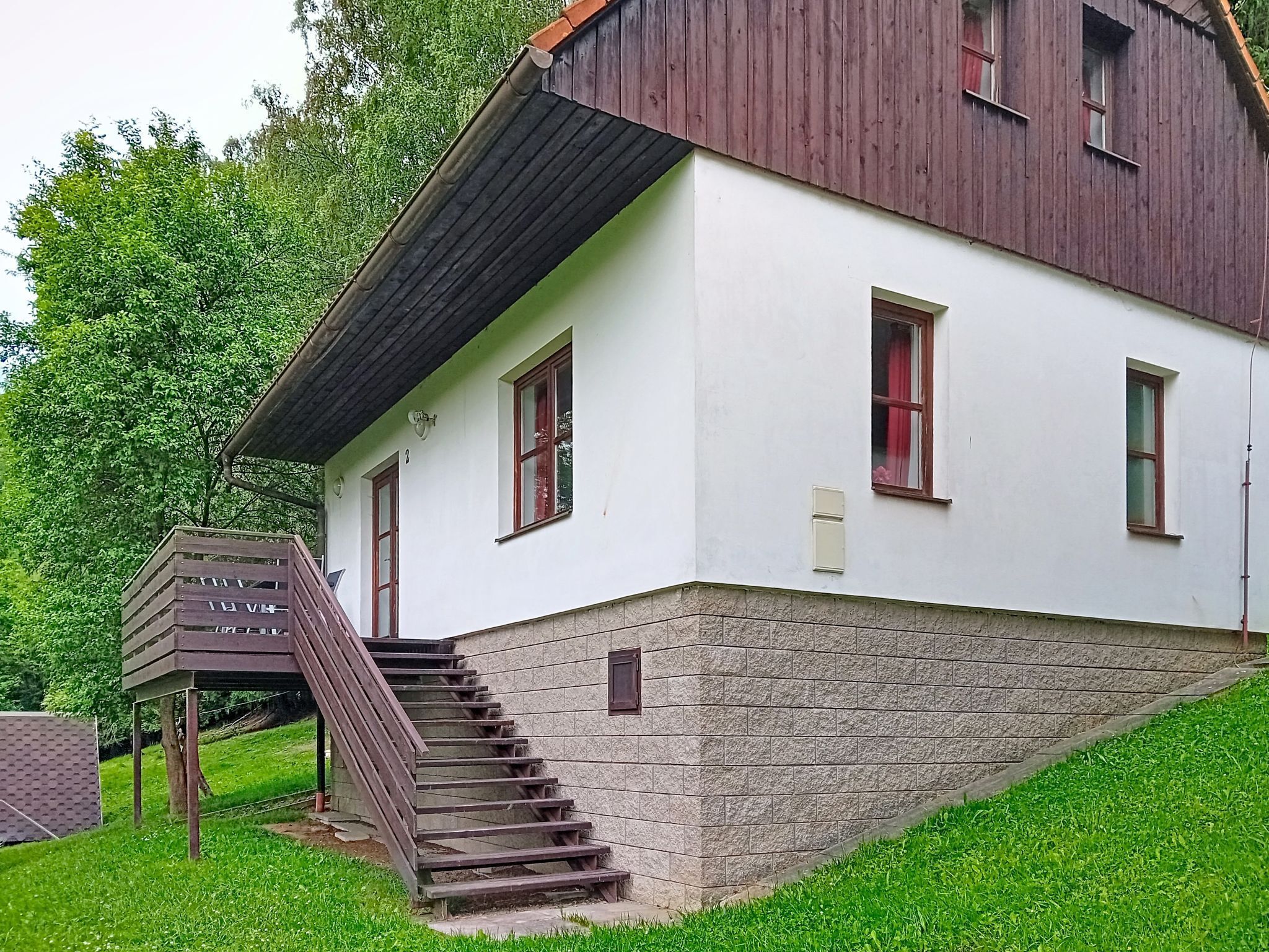 Un bâtiment à deux étages, avec une base en pierre et une partie supérieure blanche, agrémenté d’un escalier en bois menant à l’entrée.