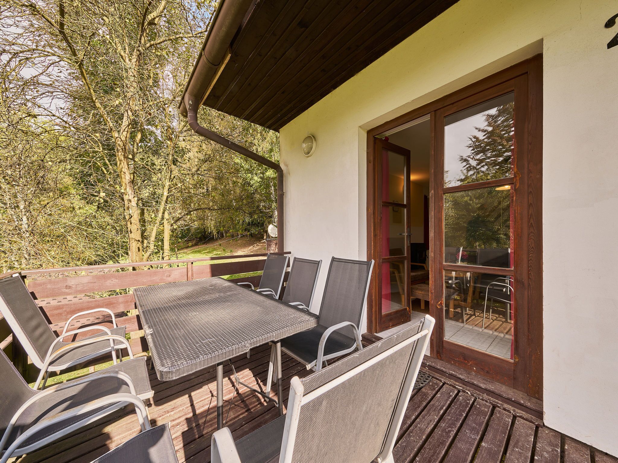 Une terrasse extérieure avec une table et des chaises, une terrasse en bois et une porte vitrée donnant sur un espace intérieur.