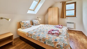 Un dormitorio con tragaluz, una cama con colcha floral, un armario de madera, una mesita de noche y un radiador.
