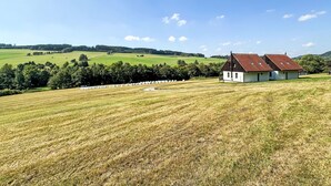A rural landscape with a white house with a red roof, surrounded by fields and trees.