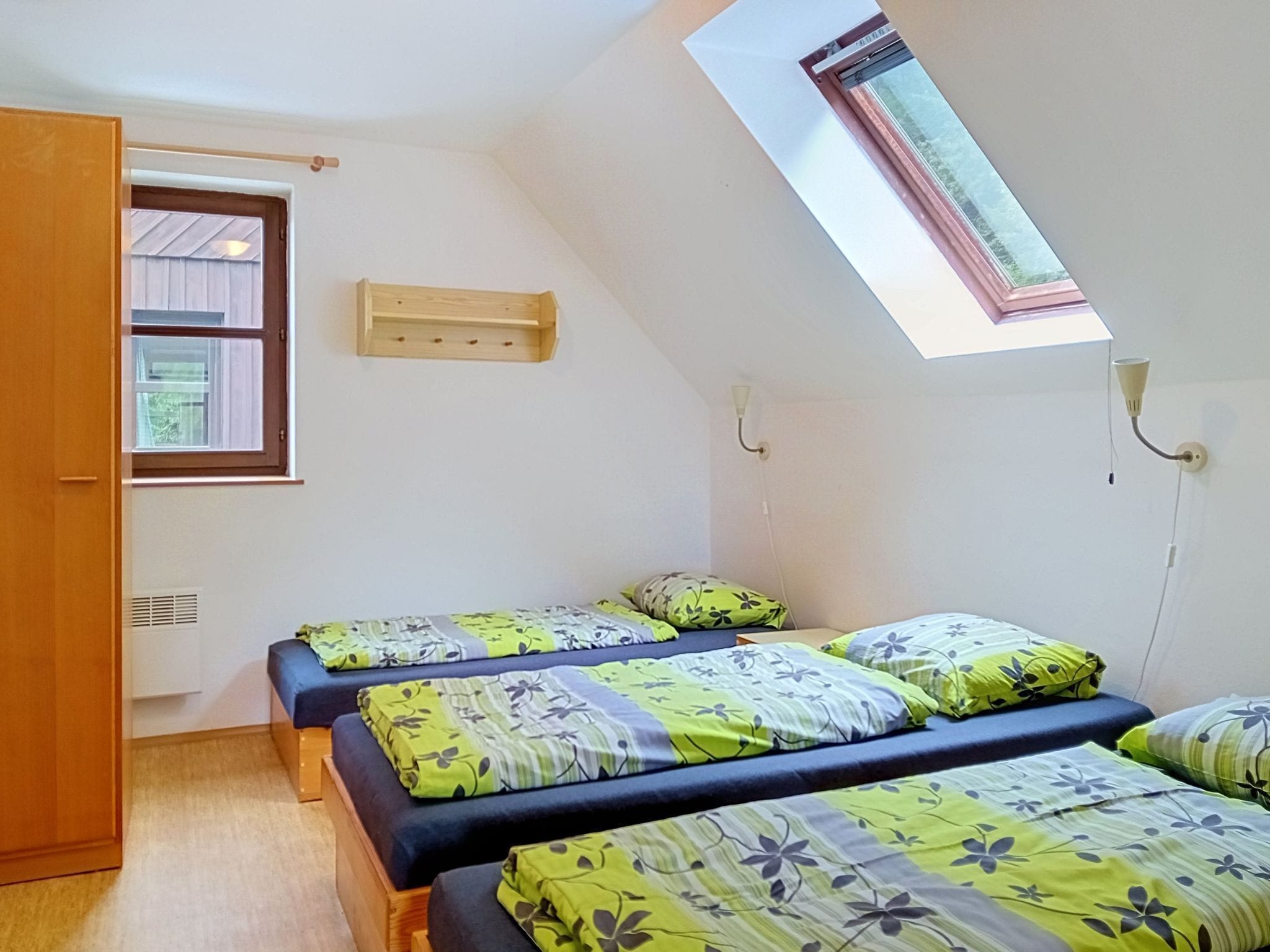 Une chambre avec deux lits, une lucarne, une fenêtre et une armoire en bois.