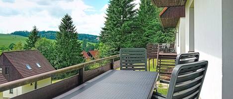 A balcony with a table and chairs, overlooking a green landscape and trees.