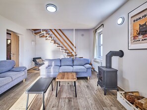 Uma sala de estar moderna com um sofá azul, uma mesa de centro de madeira, um banco preto, escadas de madeira e uma lareira a lenha.