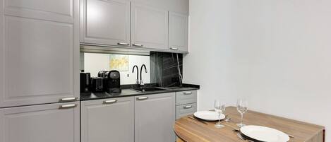 Una cocina funcional con armarios grises, encimera negra y una mesa de madera para dos personas, dispuesta con copas de vino.