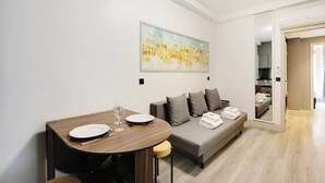Un salon moderne avec une table à manger pour deux personnes, un canapé gris agrémenté de coussins et un grand tableau abstrait accroché au mur.