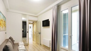 Une chambre d’hôtel moderne avec un canapé, une table à manger avec un plateau en verre et un téléviseur fixé au mur.