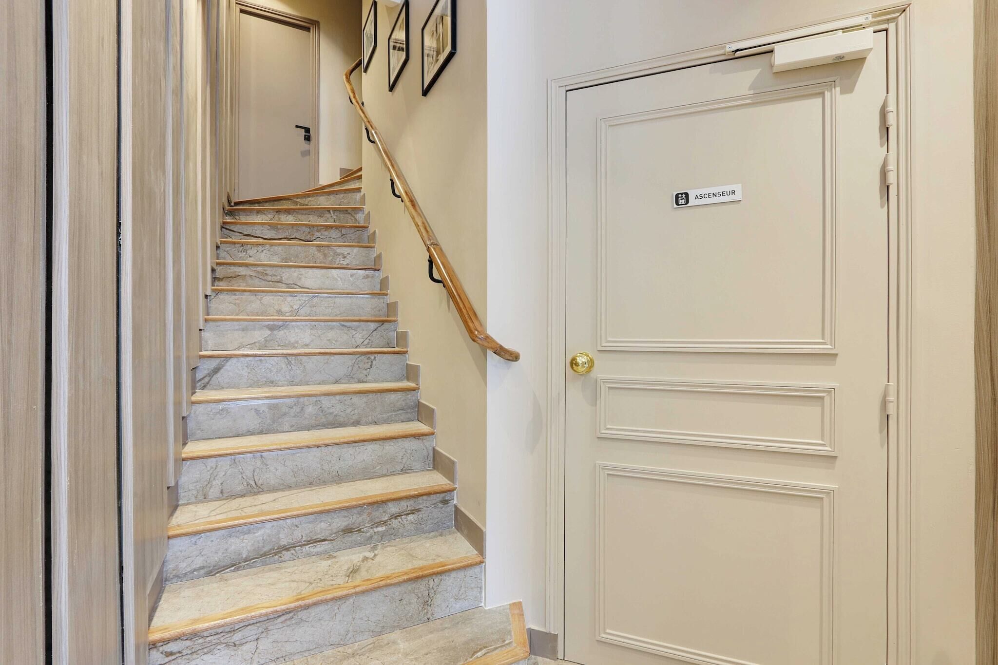 A marble staircase with a wooden handrail leading to a white door labeled "ASCENSEUR".