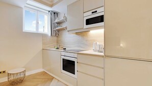 Une cuisine moderne dotée d’appareils électroménagers intégrés, d’une fenêtre avec des rideaux et d’un parquet en bois disposé en chevrons.