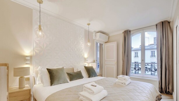 Une chambre d’hôtel avec un grand lit, des lampes de chevet, une fenêtre avec des rideaux et une vue sur les bâtiments environnants.