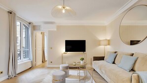 Un salon moderne avec un canapé, des poufs, un téléviseur et une lampe.