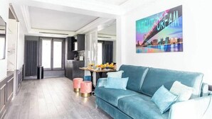 A modern living room with a teal sofa, a cityscape painting, and a kitchen area in the background.