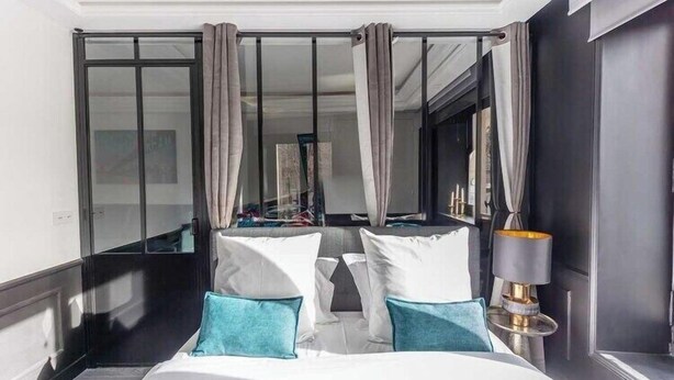 A hotel room with a bed, curtains, a lamp, and a view through a glass door.