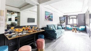 A modern hotel room with a dining area, a sofa, and a TV.