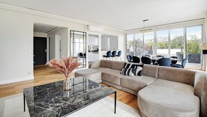 A modern living room with a sectional sofa, a glass coffee table, and a view of the dining area. - Stunning apartment - 3BR/6P - La DÃ©fense (Courbevoie)