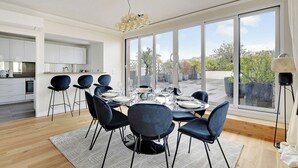 A modern dining area with a large table set for six, surrounded by dark chairs, in a bright room with large windows offering a view of the outdoors. - Stunning apartment - 3BR/6P - La DÃ©fense (Courbevoie)