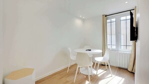 A room with a round table and four white chairs, a radiator, and a window with curtains.