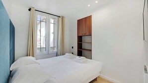 A bedroom with a bed, a window with curtains, a wooden wardrobe, and a white wall.