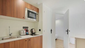 A compact kitchen with wooden cabinets, a microwave, a toaster, and a kettle.