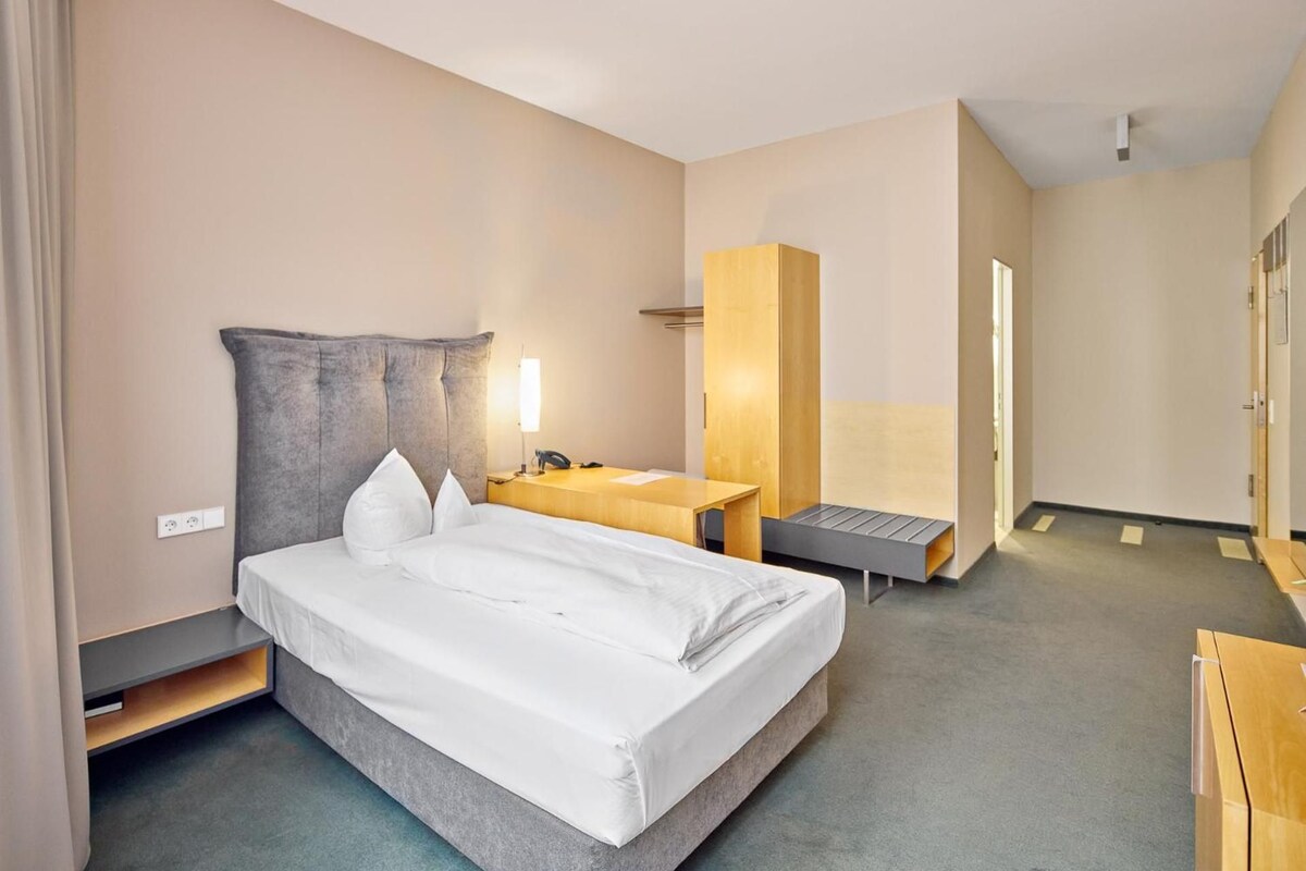 Habitació d'hotel amb llit, taula de nit, làmpada i armari.