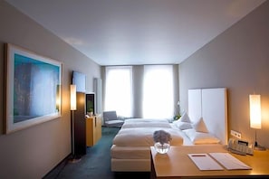 A hotel room with a bed, bedside table, lamp, and a painting on the wall.