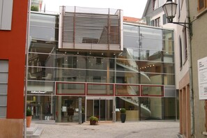 A modern building with a glass facade, a visible entrance, and a staircase leading to an upper level.
