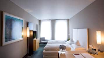 A hotel room with two beds, a desk with a telephone and papers, a chair, a large painting, and a radiator.