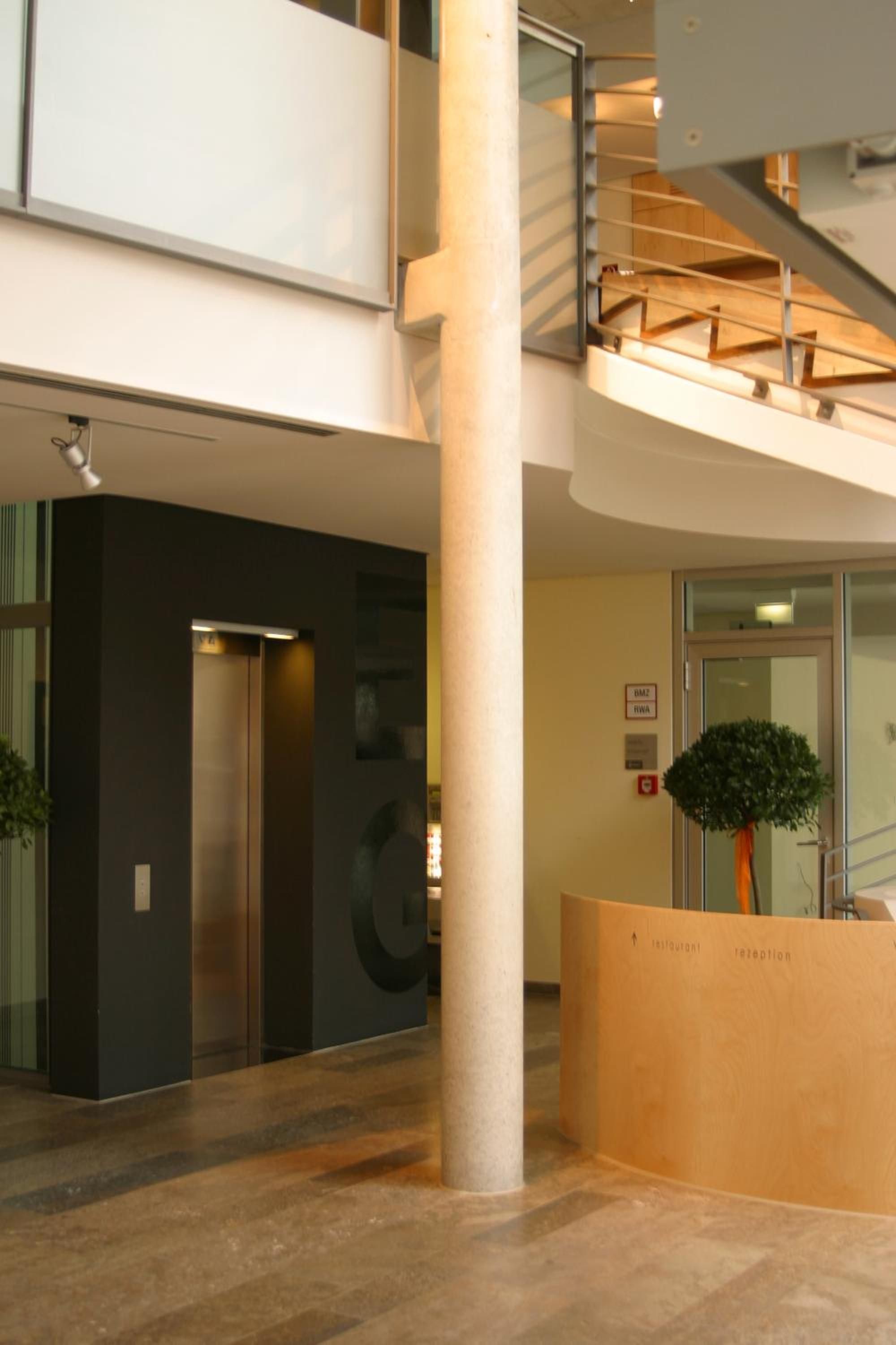 A modern interior with a reception desk, a staircase, and an elevator.