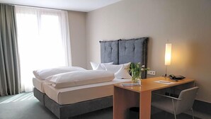 A hotel room with a bed, bedside table, lamp, and a chair.