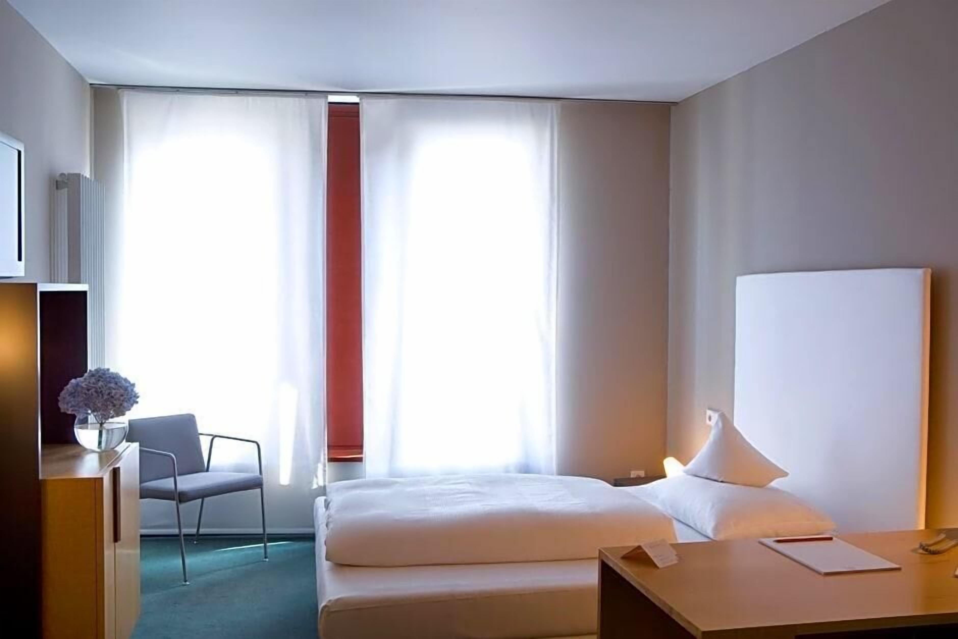 A hotel room with a bed, a desk, a chair, and a window with curtains.