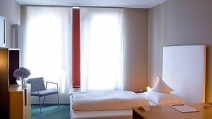 A hotel room with a bed, a desk, a chair, and a window with curtains.