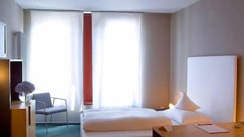 A hotel room with a bed, a desk, a chair, and a window with curtains.