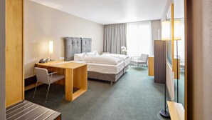 A hotel room with a bed, desk, chair, and a large mirror.