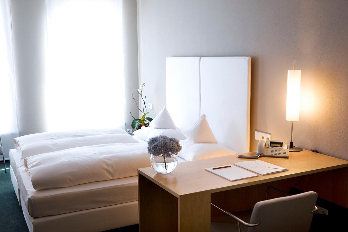 Habitació d'hotel amb un llit, una taula de nit, una cadira, una làmpada i un telèfon.