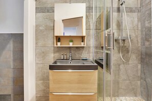 A modern bathroom with a glass-enclosed shower, a built-in sink with a mirror above, and a shelf with decorative items.