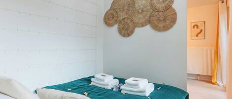 A hotel room with a bed, teal bedspread, white pillows, and a wall with woven wall art.