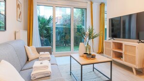 Uma sala de estar moderna com um sofá cinzento, uma mesa de centro, uma TV sobre um armário de madeira e uma grande porta de vidro deslizante que dá para um jardim.