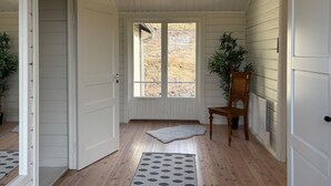 Un corridoio con pavimento in legno, una porta bianca, una finestra vista su un paesaggio arido, una sedia di legno e due tappeti.