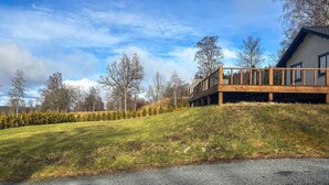 Una casa moderna con un patio in legno e una strada privata in pendenza.